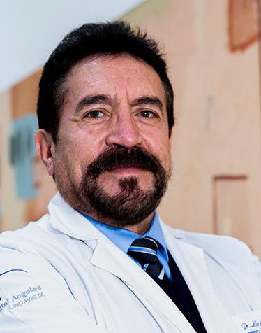 Es la foto de perfil de un ginecólogo y obstetra en Ciudad de México de Hospital Angeles Lindavista. Tiene el cabello, barba y bigote negro. Usa una bata blanca, un suéter, una camisa azul y una corbata azul con rayas.