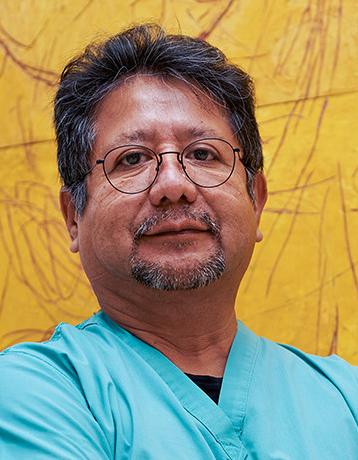 Es la foto de perfil de un urólogo en Ciudad de México de Hospital Angeles Lindavista. Tiene el cabello y barba negra. Usa lentes y un uniforme médico azul claro. Está sonriendo.