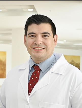 Es la foto de perfil de un geriatra en Ciudad Juárez de Hospital Angeles Ciudad Juárez. Utiliza una camisa azul con corbata roja y una bata blanca.