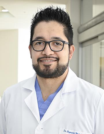 Es la foto de perfil de un cirujano general en Ciudad Juárez de Hospital Angeles Ciudad Juárez. Utiliza bata blanca, con uniforme azul cielo debajo.