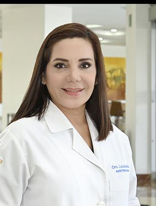 Es la foto de perfil de un anestesiólogo en Ciudad Juárez de Hospital Angeles Ciudad Juárez. La doctora tiene el cabello castaño oscuro, lacio y suelto. Está sonriendo y viste una bata médica blanca con su nombre y la especialidad 'Anestesiología' bordados en el pecho. El fondo muestra un área luminosa del hospital, con paredes claras y una pintura en tonos cálidos.