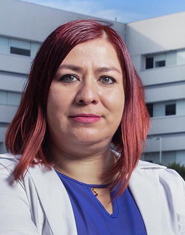 Es la foto de perfil de una internista y geriatra en Ciudad de México de Hospital Angeles. La doctora tiene el cabello rojo, ojos verdes, viste una blusa azul eléctrico y una bata blanca. 