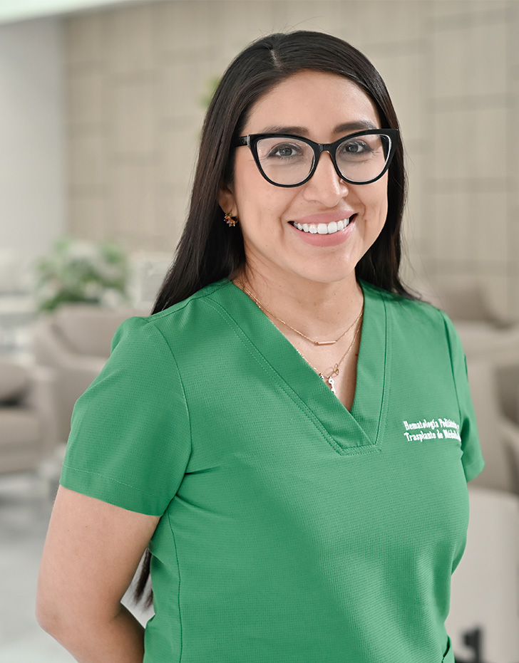 Es la foto de perfil de una hematología pediátrica en Querétaro de Hospital Angeles Centro Sur. Viste un uniforme verde, tiene joyería dorada, está sonriendo y es de tez morena con cabello oscuro y largo.