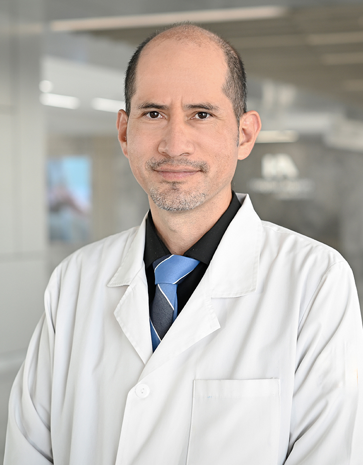 Es la foto de perfil de un pediatra en Querétaro de Hospital Angeles Centro Sur. Usa bata blanca con una camisa negra y corbata azul, está sonriendo.