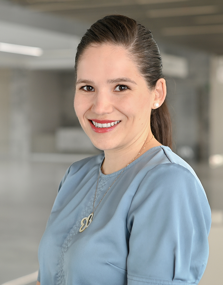 Es la foto de perfil de una cirujana general en Querétaro de Hospital Angeles Centro Sur. Usa una blusa azul y un collar dorado en forma del contorno de una mariposa. Tiene una coleta y está sonriendo.