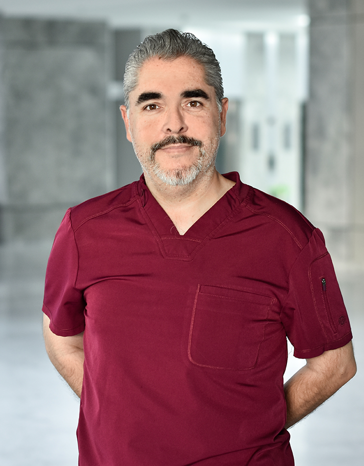 Es la foto de perfil de un cirujano general en Querétaro de Hospital Angeles Centro Sur. Usa un uniforme vino, tiene cejas pobladas, barba y bigote y cabello canoso.