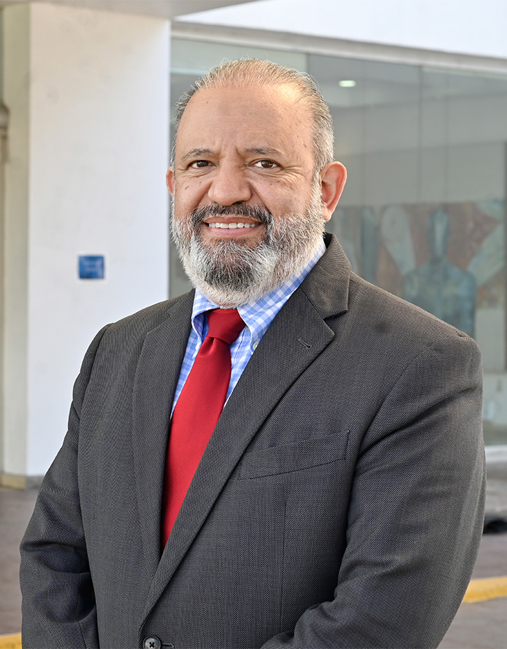 Es la foto de perfil de un otorrinolaringólogo en Tijuana de Hospital Angeles Tijuana. Usa un saco negro con una corbata roja. Tiene barba gris y está sonriendo.