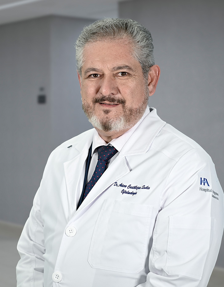 Es la foto de perfil de un oftalmólogo en Ciudad de México de Hospital Angeles Lindavista. Tiene el bigote negro, además de barba y cabello gris. Usa una bata blanca con una camisa azul.