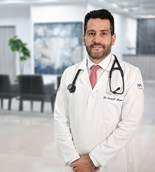 Es la foto de perfil de un cardiólogo en Ciudad de México de Hospital Angeles. Tiene una bata blanca, camisa azul y corbata roja, tiene barba, bigote y cejas pobladas, su cabello es rizado.