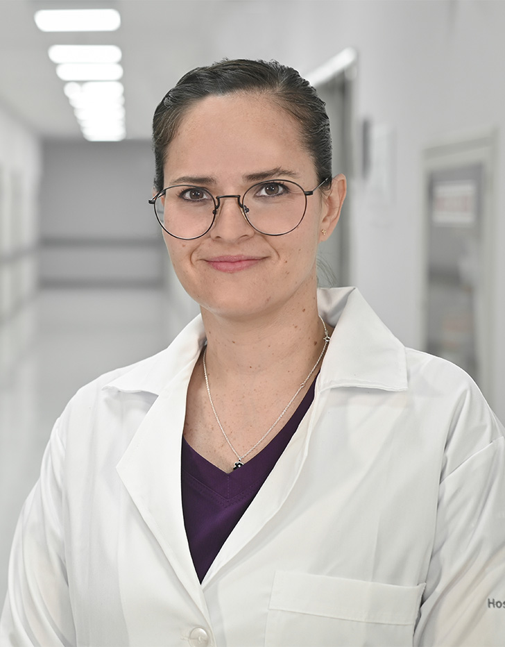 Es la foto de perfil de una otorrinolaringóloga en Ciudad de México de Hospital Angeles Universidad. Usa una bata blanca con blusa vino. Usa lentes y cabello recogido.