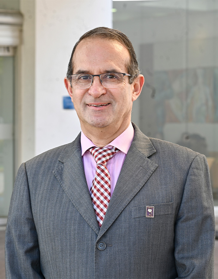 Es la foto de perfil de un anestesiólogo en Tijuana de Hospital Angeles Tijuana.Usa un traje gris con una camisa rosa y una corbata de cuatros. Usa lentes.