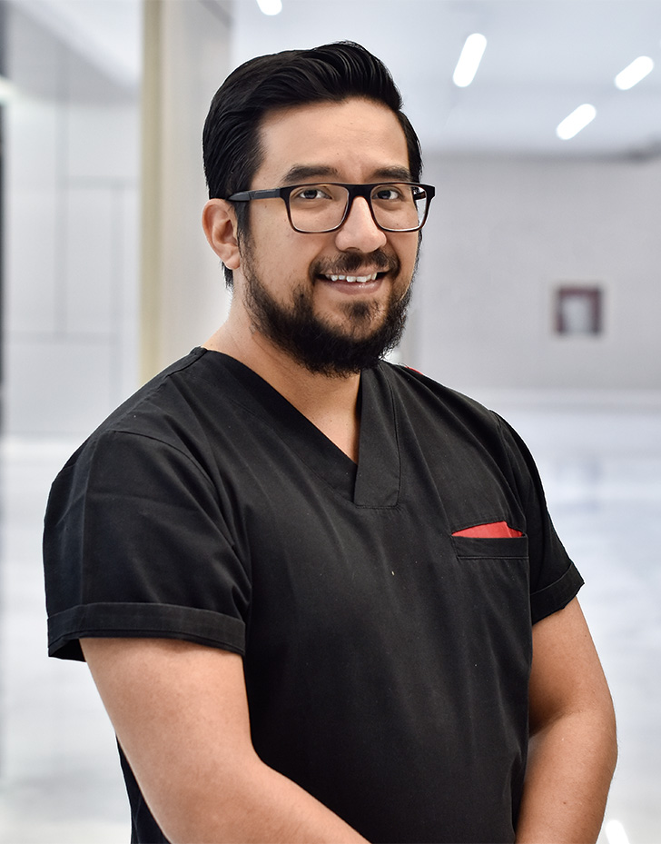 Es la foto de perfil de un cirujano oncológico en Querétaro de Hospital Angeles Centro Sur. está sonriendo, tiene lentes y barba. Usa un uniforme negro.