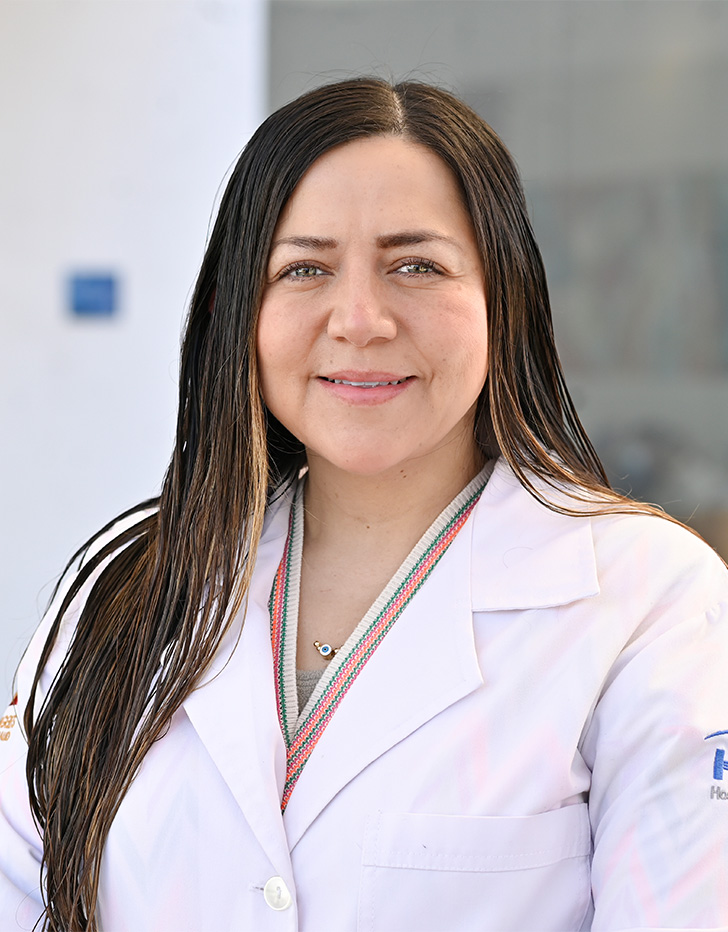 Es la foto de perfil de un dermatólogo pediátrico en Tijuana de Hospital Angeles Tijuana. Usa una bata blanca. Tiene el cabello café y lacio.