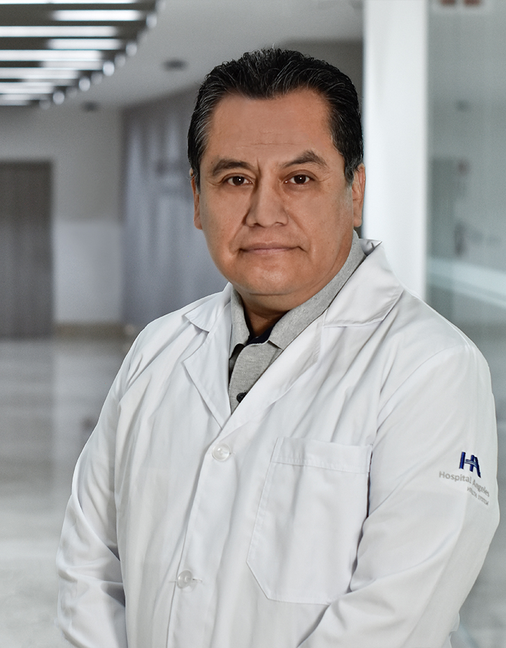 Es la foto de perfil de un anestesiólogo en Huixquilucan de Hospital Angeles Lomas. Usa una bata blanca, tiene camisa gris, es de tez morena y su cabello es negro.