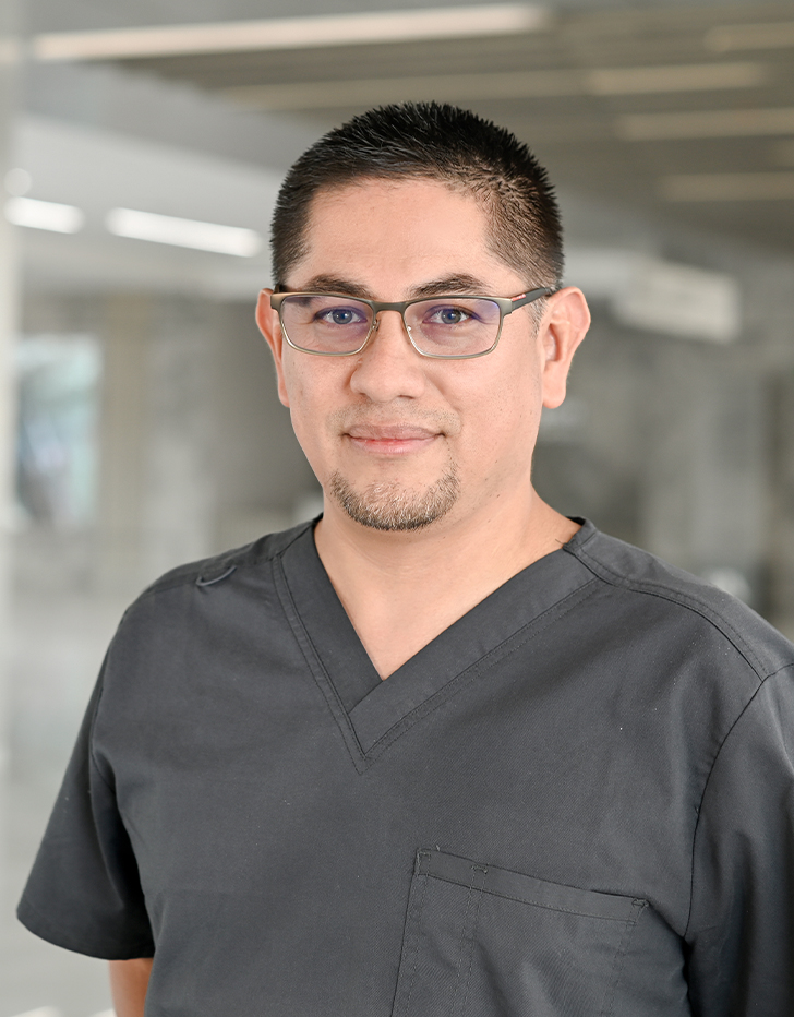 Es la foto de perfil de un ginecólogo y obstetra en Querétaro de Hospital Angeles Centro Sur. Usa un uniforme gris de cuello V y lentes.