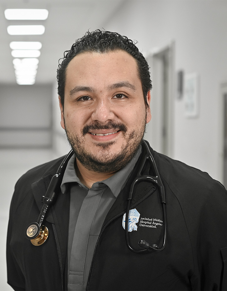 Es la foto de perfil de un especialista en medicina crítica en Ciudad de México de Hospital Angeles Universidad. Usa una chamarra negra con un estetoscopio en el cuello y una camisa gris. Tiene la barba, cabello y bigote negro.