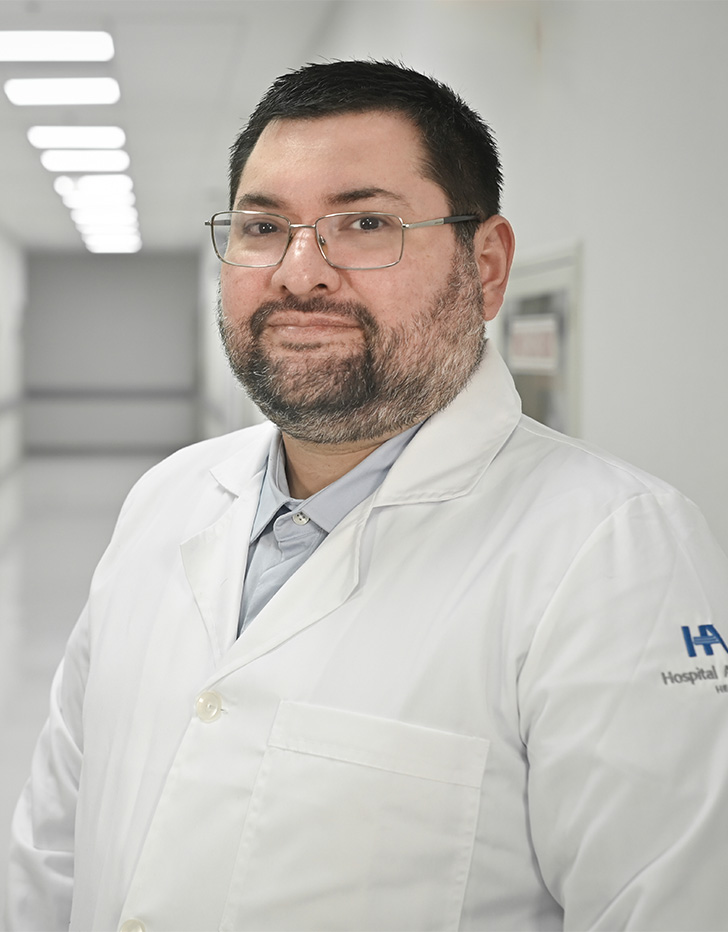 Es la foto de perfil de un cirujano cardiotorácico en Ciudad de México de Hospital Angeles. El doctor viste una bata blanca, camisa gris claro, tiene barba y lentes plateados.