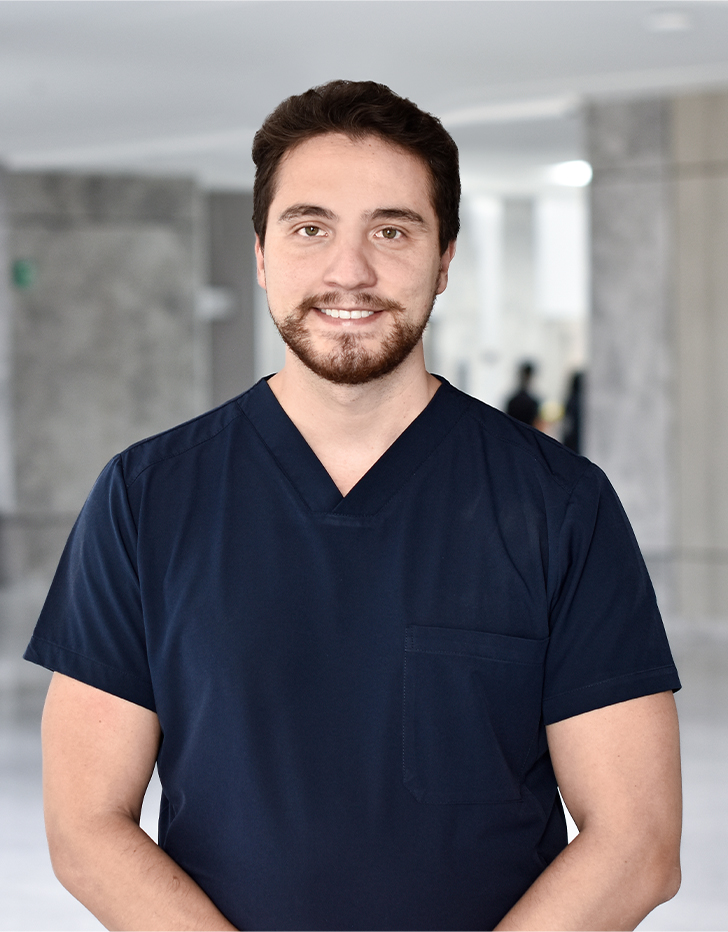 Es la foto de perfil de un cirujano maxilofacial en Querétaro de Hospital Angeles Centro Sur. está sonriendo, tiene barba y un uniforme azul rey.