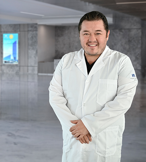Es la foto de perfil de un oftalmólogo en Querétaro de Hospital Angeles Centro Sur. Viste un uniforme verde olivo, está sonriendo y de fondo se ve el pasillo del hospital.