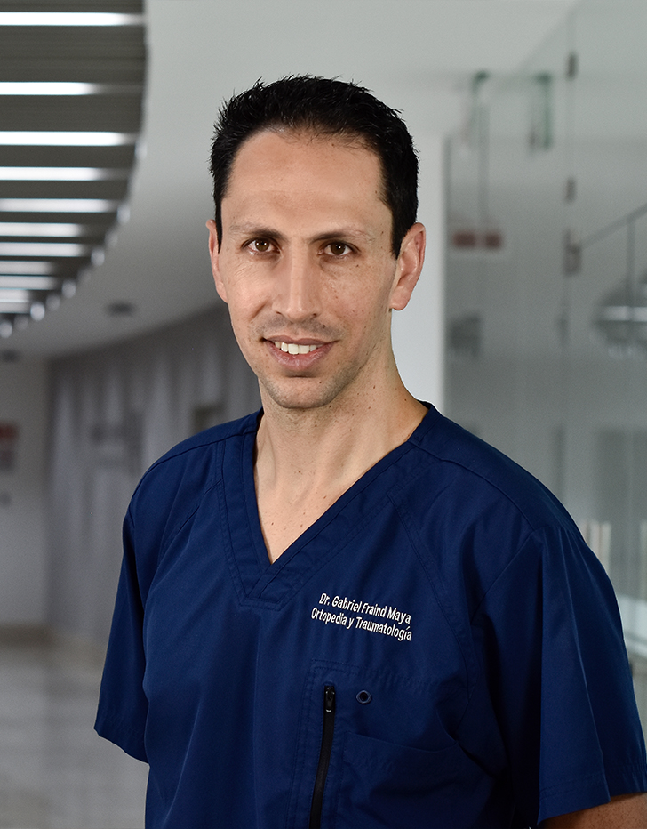 Es la foto de perfil de un ortopedista y traumatólogo en Huixquilucan de Hospital Angeles Lomas. Tiene un uniforme azul marino con cuello V. Es de tez morena y está sonriendo.