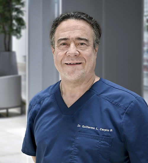 Es la foto de perfil de un ginecólogo y obstetra en Huixquilucan de Hospital Angeles Lomas. Usa un uniforme azul, tiene el cabello ligeramente largo, tiene los brazos cruzados y está sonriendo.