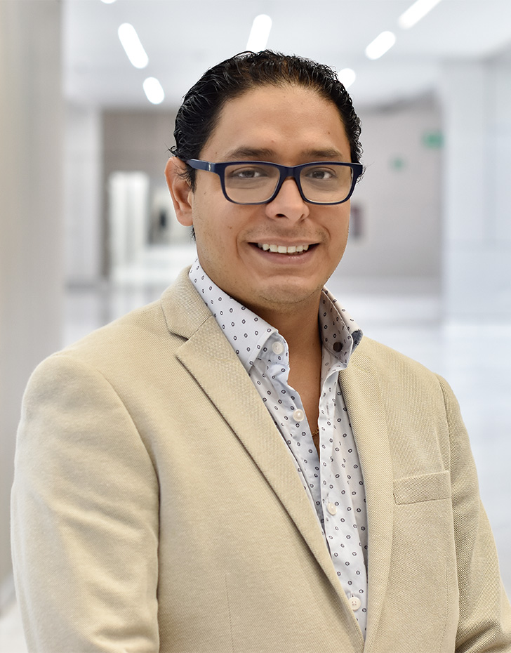 Es la foto de perfil de un neumólogo en Querétaro de Hospital Angeles Centro Sur. Viste un traje beige con una camisa negra y lunares negros. Usa lentes y está sonriendo.