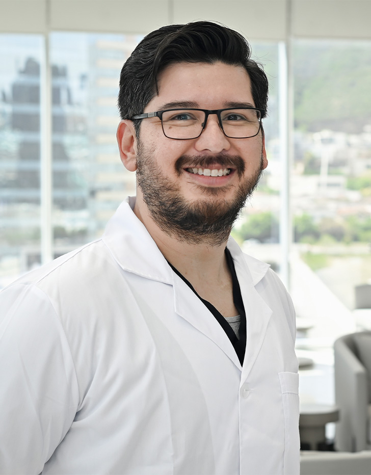 Es la foto de perfil de un coloproctólogo y cirujano general en San Pedro Garza de Hospital Angeles Valle Oriente. Usa una bata blanca y lentes. Tiene el cabello y barba negro. Está sonriendo.