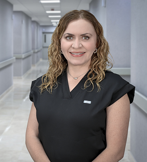 Es la foto de perfil de una ginecóloga y obstetra en León de Hospital Angeles León. Utiliza una bata blanca con una camisa azul marino y líneas. Tiene el cabello castaño claro.