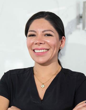 Es la foto de perfil de una cirujana general en Ciudad de México de Hospital Angeles Lindavista. Tiene el cabello negro y recogido en una coleta. Usa un uniforme médico color negro y un collar plata. Está sonriendo y tiene los brazos cruzados.