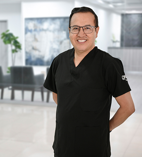 This is the profile photo of a urologist México  Hospital Angeles in México City. The doctor is wearing a blue scrub, smiling, and wearing glasses.