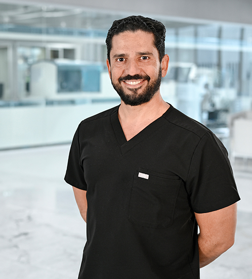 Es la foto de perfil de un cirujano general en Guadalajara de Hospital Angeles Del Carmen. Utiliza un uniforme azul, tiene barba y bigote y cabello negro.