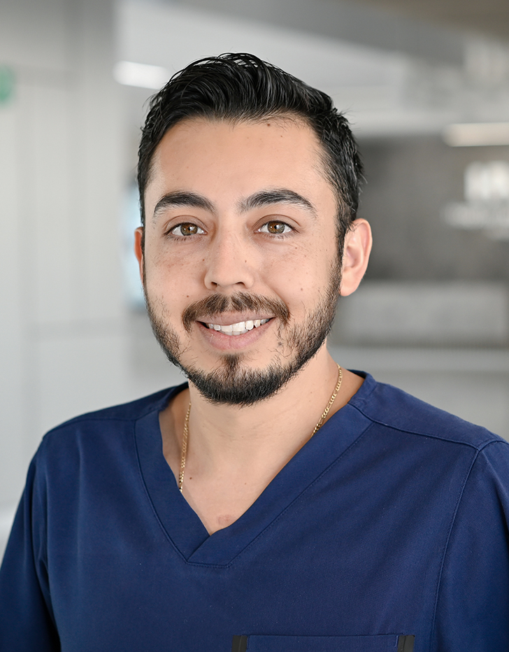 Es la foto de perfil de un cirujano general en Querétaro de Hospital Angeles Centro Sur. está usando un uniforme azul marino, tiene una cadena dorada, barba y bigote y cejas pobladas.