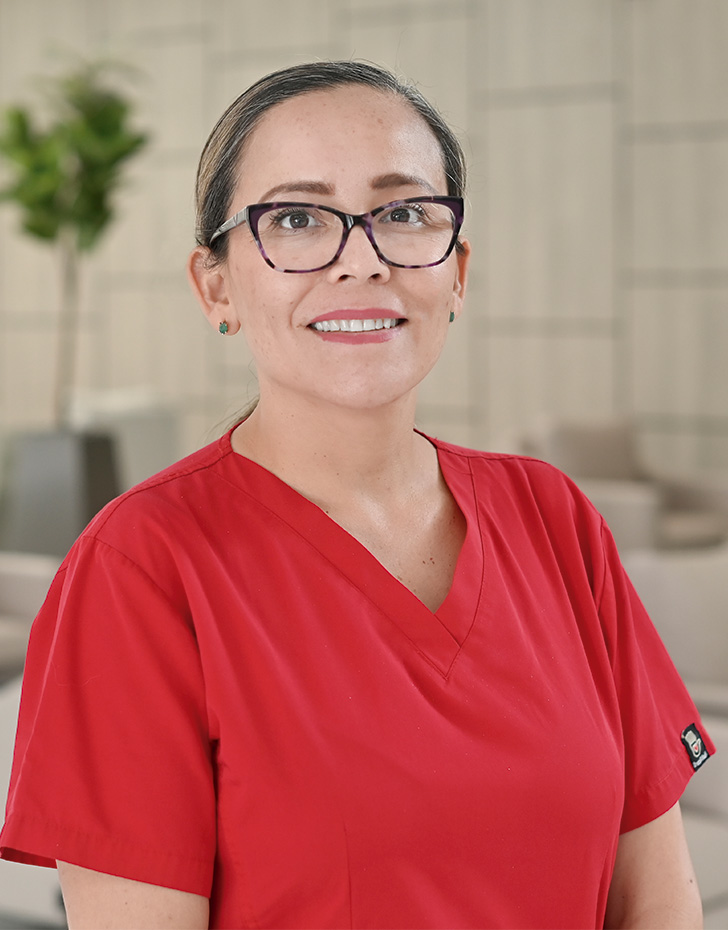 Es la foto de perfil de una anestesióloga en Querétaro de Hospital Angeles Centro Sur. Usa un uniforme rojo, tiene lentes cuadrados y aretes verde.