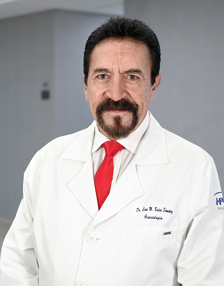 Es la foto de perfil de un ginecólogo y obstetra en Ciudad de México de Hospital Angeles Lindavista. Tiene el cabello, barba y bigote negro. Usa una bata blanca, un suéter, una camisa azul y una corbata azul con rayas.