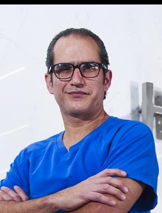 Es la foto de perfil de un ginecólogo oncológico en Ciudad de México de Hospital Angeles. El doctor tiene un uniforme azul, usa lentes de marco negro y está sonriendo suavemente. 