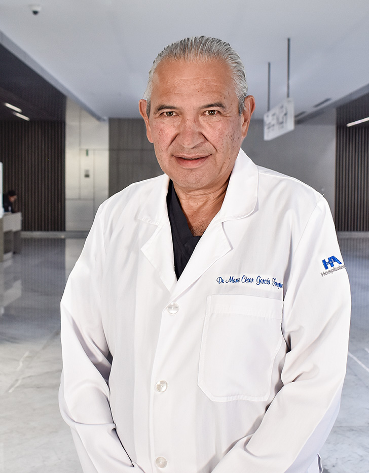 Es la foto de perfil de un especialista en cirugía general y gastrocirugía en Querétaro de Hospital Angeles Centro Sur. El doctor tiene una bata blanca una playera azul marino y cabello peinado hacia atrás. 