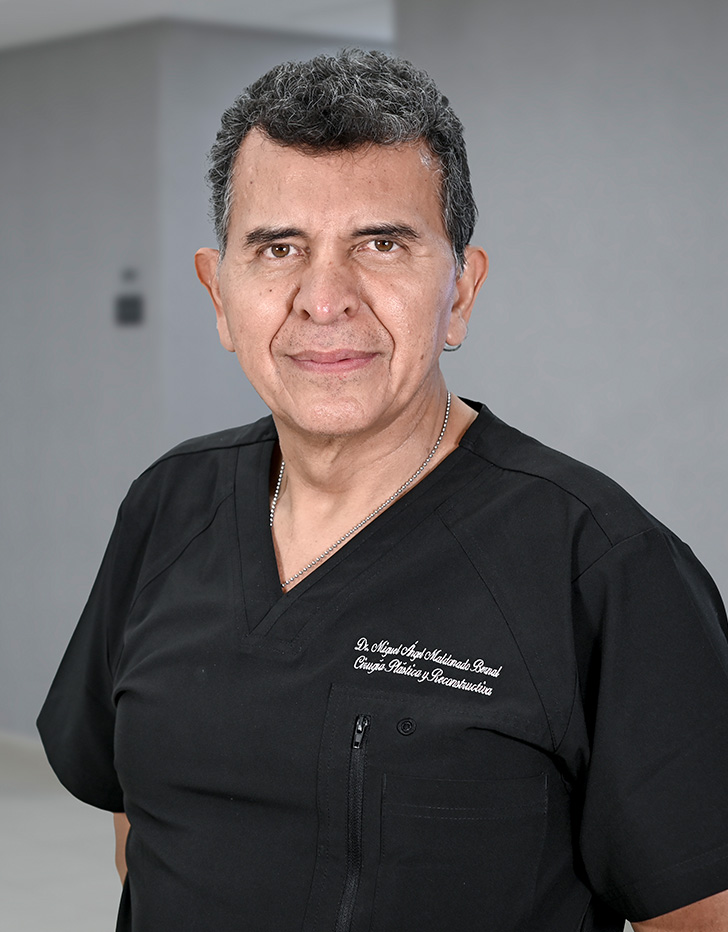 Es la foto de perfil de un cirujano plástico en Ciudad de México de Hospital Angeles Lindavista. Tiene el cabello gris. Usa una bata blanca, una camisa azul claro y una corbata azul más oscuro. Está sonriendo.