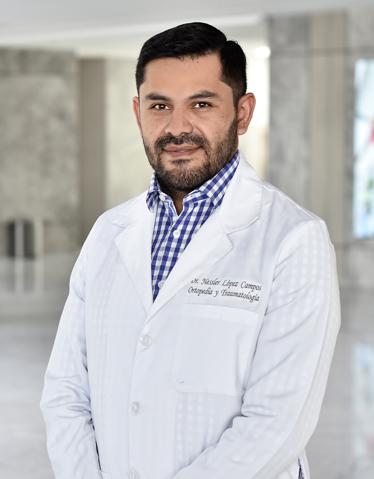 Es la foto de perfil de un ortopedista y traumatólogo en Querétaro de Hospital Angeles Centro Sur. El doctor tiene una bata blanca con una camisa azul con cuadros blancos el doctor tiene un uniforme negro y está sonriendo.