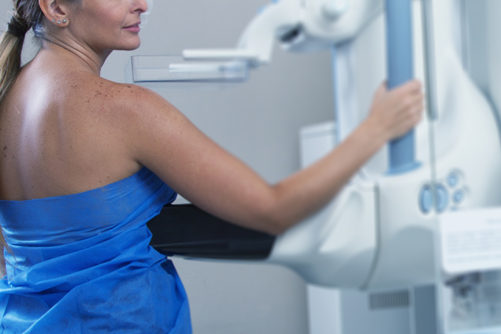 Mujer en bata azul de espaldas, sostenida de un equipo durante un estudio mamario.