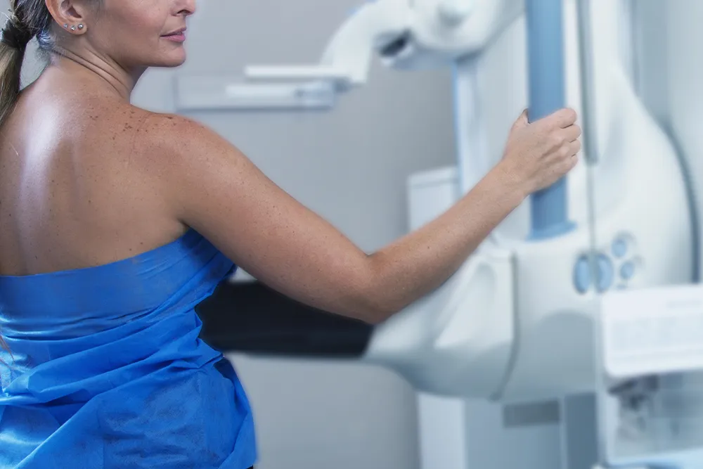 Mujer de espaldas con bata azul recargando la mama durante una mastografía.
