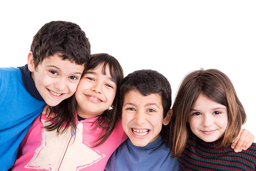 Cuatro niños con sueter de colores, abrazados y sonriendo sobre fondo blanco.