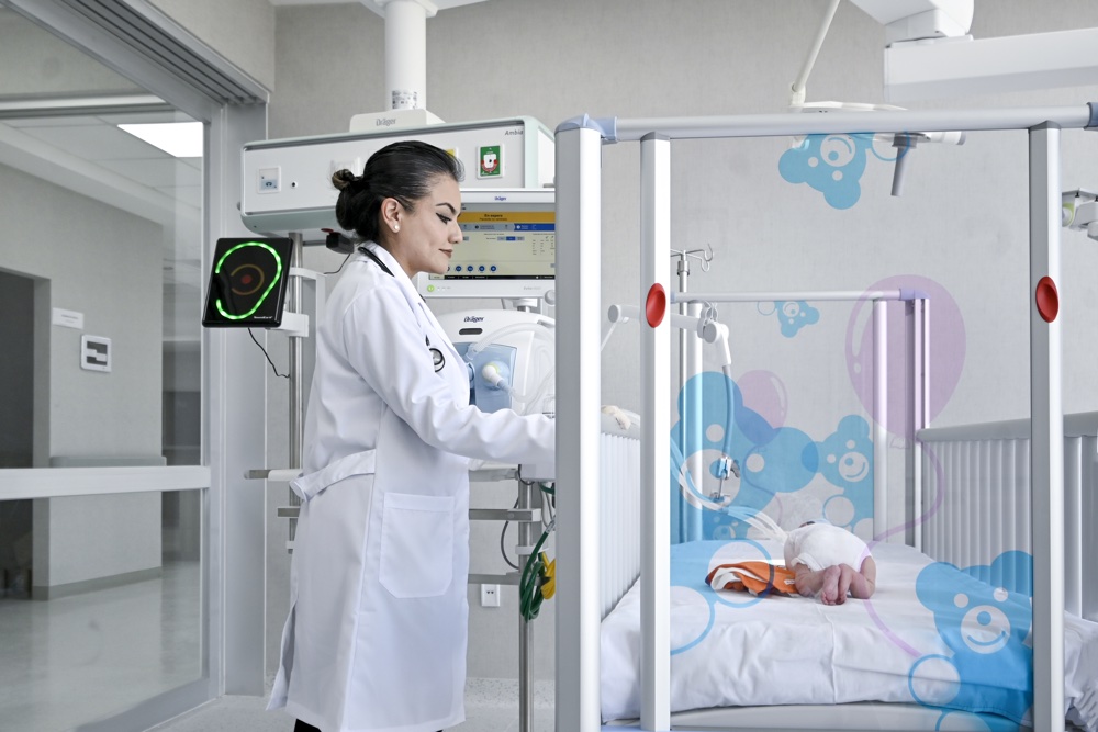 Doctora con bata blanca monitoreando a un bebé recién nacido en el área de cuidados intensivos pediatricos